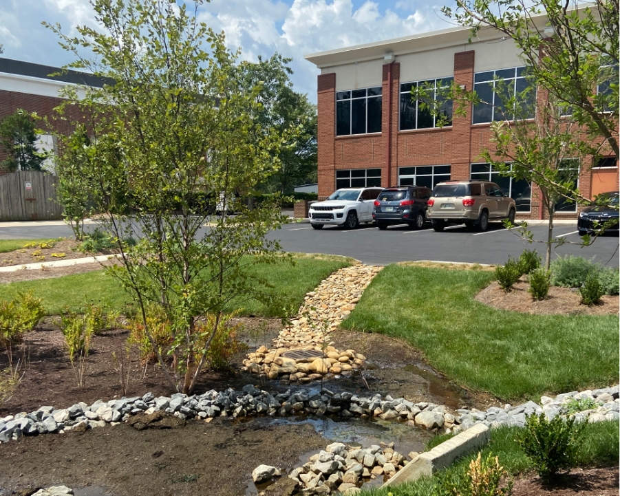 Landscaped stormwater management area with a rock-lined drainage feature leading to a brick commercial building, showcasing M2 Group's civil engineering expertise.