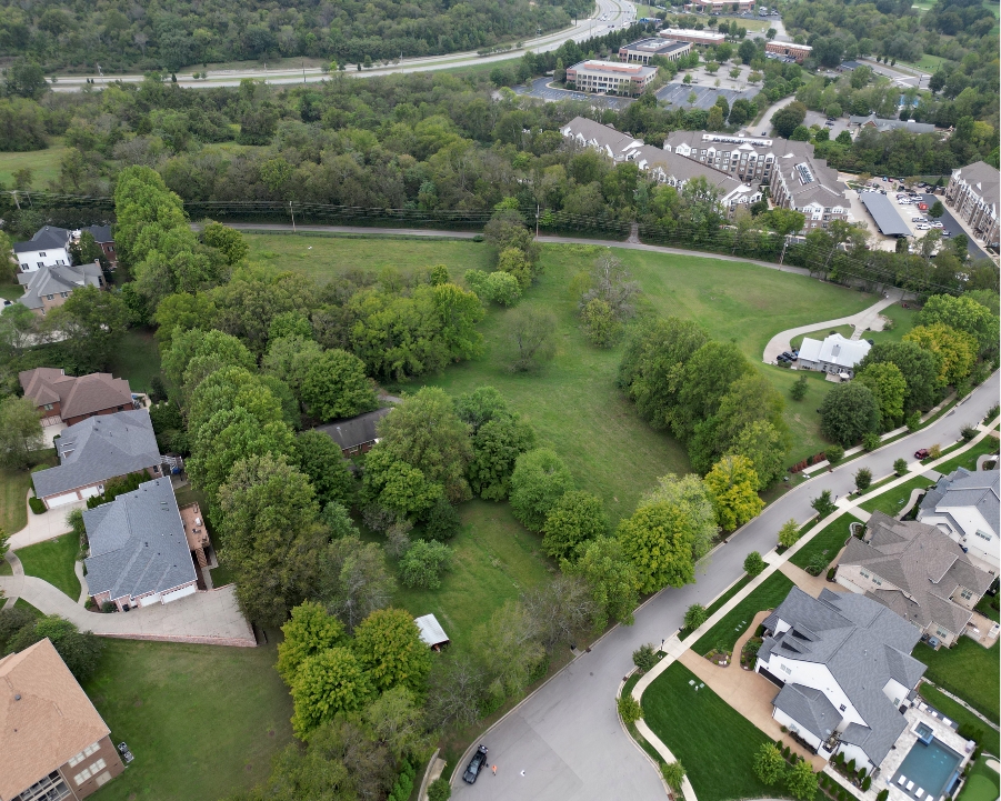 Aerial view of a residential area with grassy lawns, trees, and rooftops of homes.