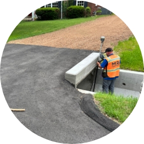 Worker in an orange vest standing inside a storm drain culvert, using a land surveying instrument on a tripod, representing M2 Group's stormwater infrastructure project expertise