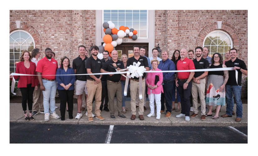 M2 Group ribbon-cutting ceremony featuring team members and partners in front of a brick building with decorative balloons.