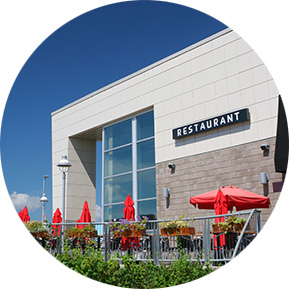 Modern restaurant with an outdoor patio featuring red umbrellas and flower planters, representing hospitality and dining spaces